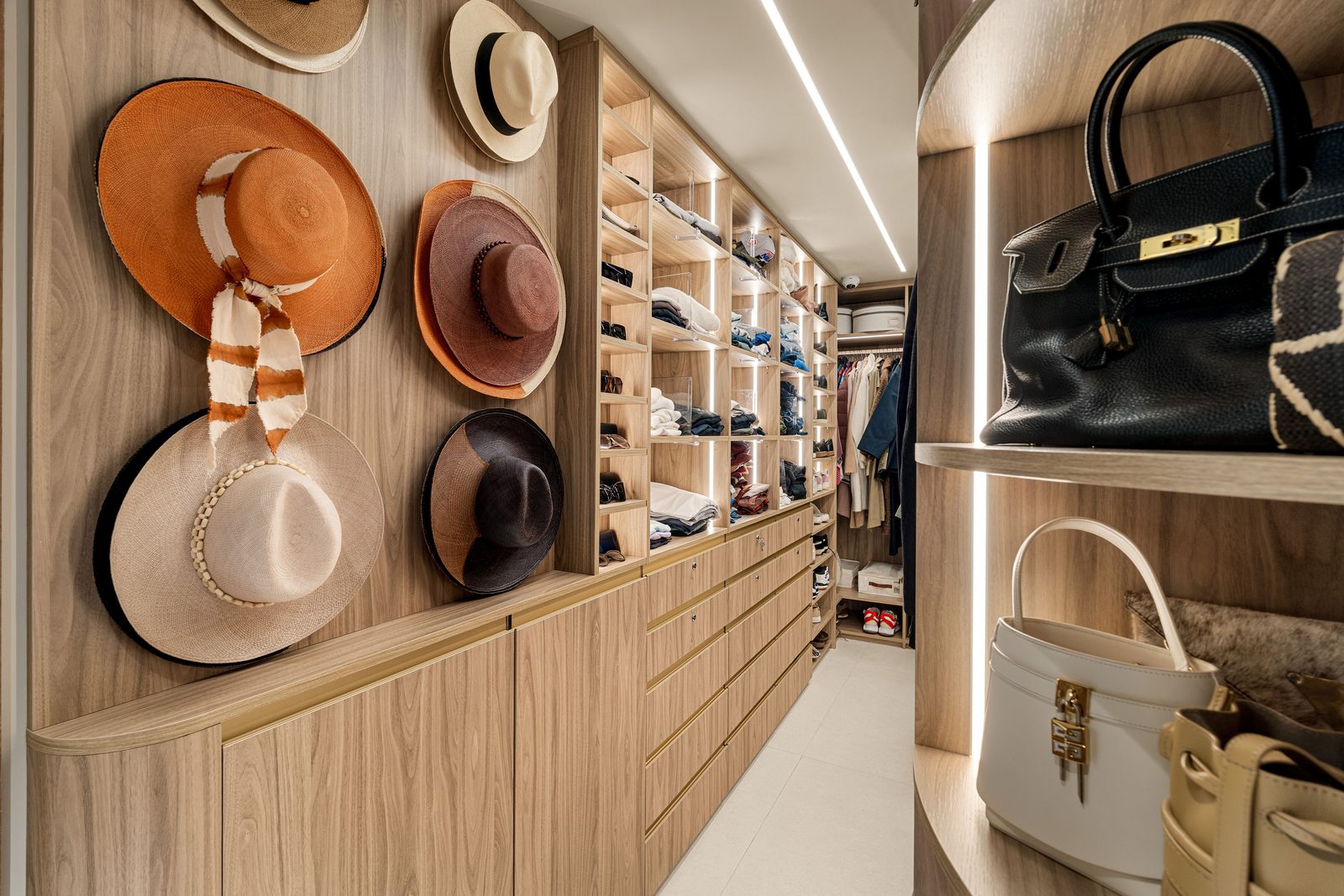Walk-in closet with a hat display wall, lit open shelving, drawer banks and curved handbag shelves