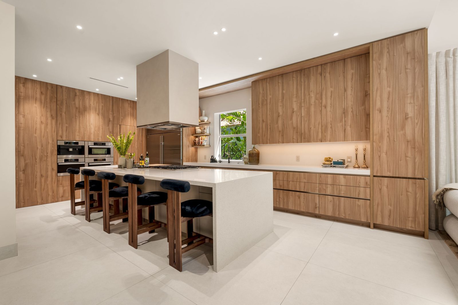 Custom kitchen with a full wall of wood cabinetry, integrated ovens and a stone waterfall island with seating