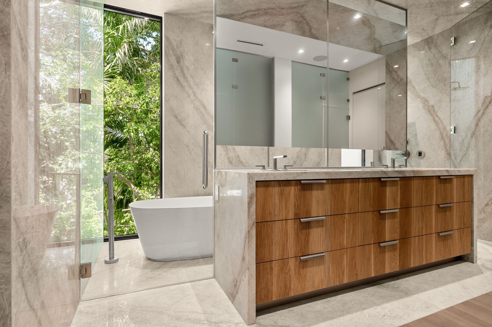 Custom double vanity with reeded wood drawer fronts and a stone countertop and waterfall end, primary bathroom